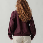Rückansicht eines weiblichen Models im bordeauxroten Half Zip.