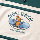 Detailaufnahme des Maus Alpine-Motivs auf dem grün-cremefarbenen Half Zip. Maus auf Skiern vor einer Bergkulisse.