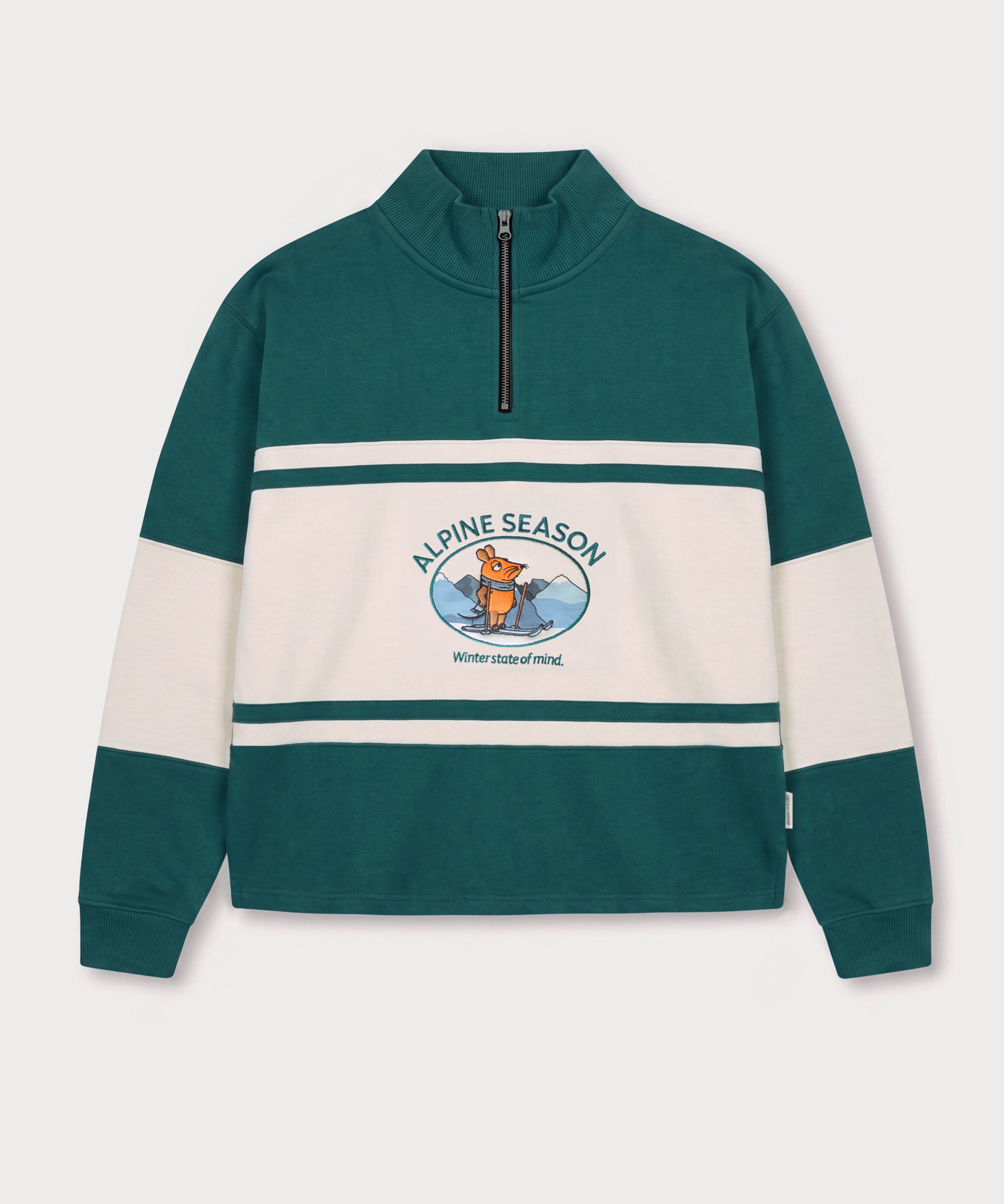 Vorderansicht des grün-cremefarbenen Half Zips mit Maus Alpine-Motiv. Maus auf Skiern vor einer Bergkulisse.