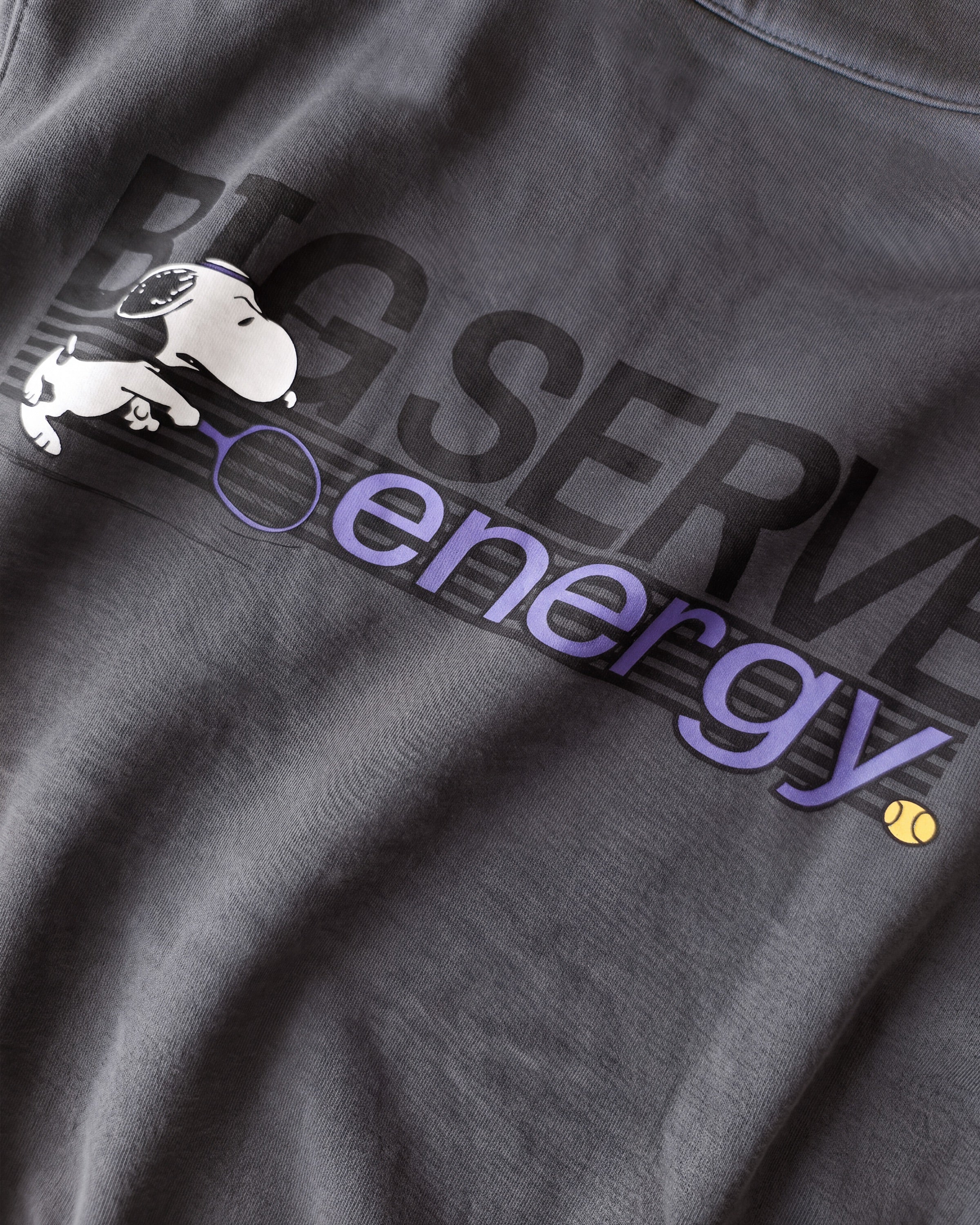Detailaufnahme des Snoopy Big Serve Energy-Rückenprints auf dem grauen Half Zip. Der hochkonzentrierte Snoopy.
