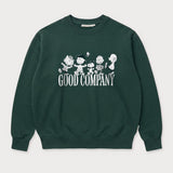 Vorderansicht des grünen Box Sweaters mit Peanuts Good Company-Print. Snoopy und seine Freunde ausgelassen tanzend über dem „GOOD COMPANY“-Schriftzug.