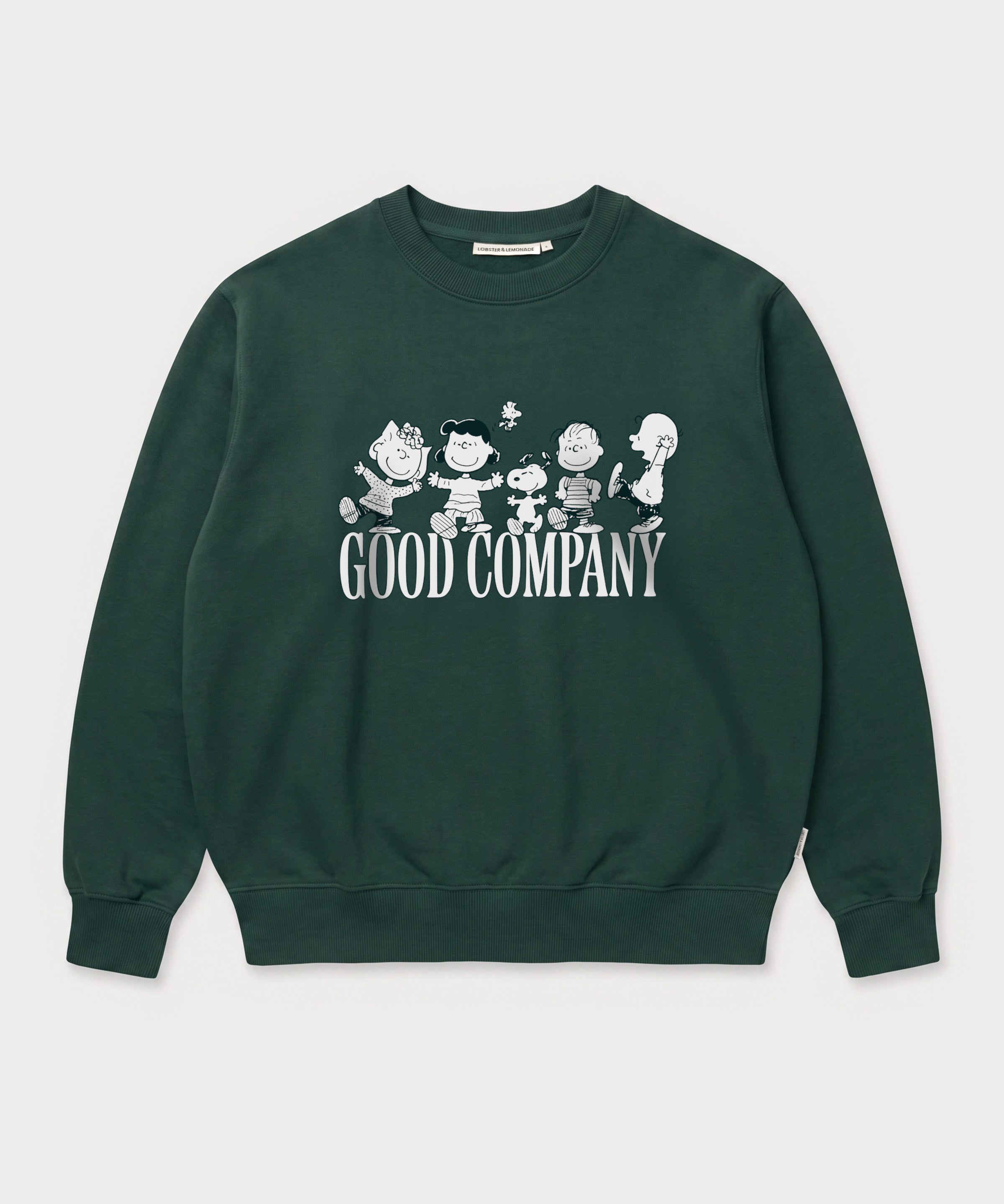 Vorderansicht des grünen Box Sweaters mit Peanuts Good Company-Print. Snoopy und seine Freunde ausgelassen tanzend über dem „GOOD COMPANY“-Schriftzug.