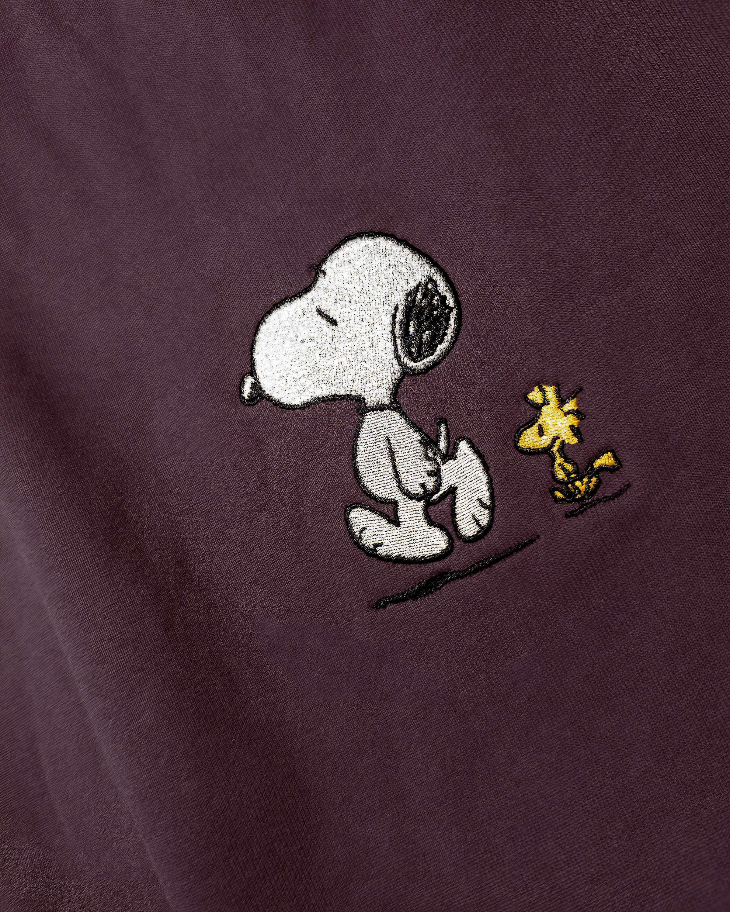 Detailaufnahme der Snoop Läuft-Stickerei auf dem bordeauxroten Hoodie. Der entspannte Snoopy, der gemeinsam mit Woodstock spaziert.