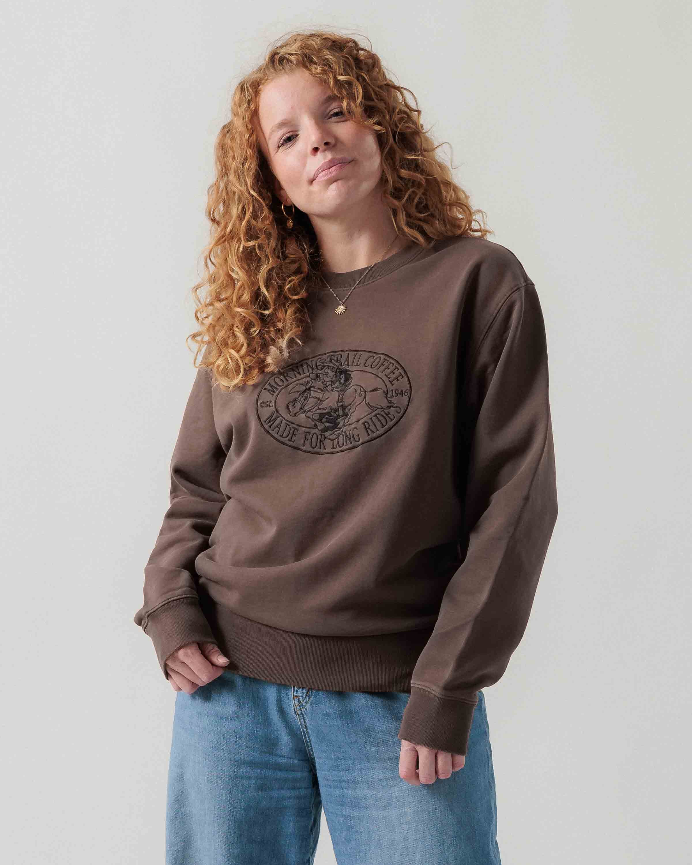 Vorderansicht eines weiblichen Models im braunen Box Sweater mit Lucky Luke Coffee Run-Stickerei.