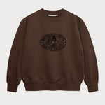 Vorderansicht des braunen Box Sweaters mit Lucky Luke Coffee Run-Stickerei. Lucky Luke, der auf Jolly Jumper reitend seinen Kaffee trinkt.