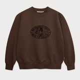 Vorderansicht des braunen Box Sweaters mit Lucky Luke Coffee Run-Stickerei. Lucky Luke, der auf Jolly Jumper reitend seinen Kaffee trinkt.