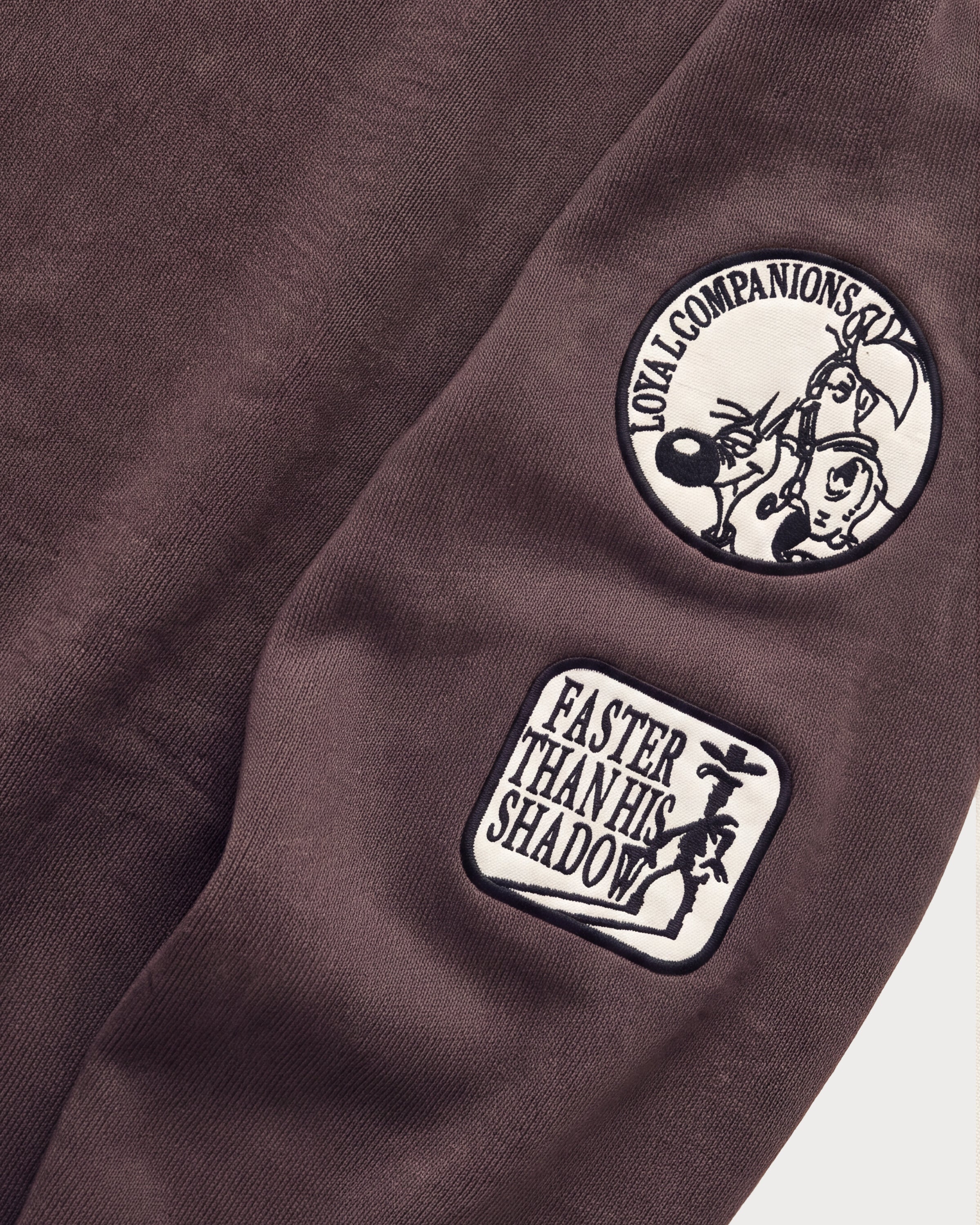 Detailaufnahme der Ärmel-Badges am braunen Boxer Hoodie.