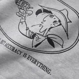 Detailaufnahme der Lucky Luke Accuracy-Stickerei auf dem grauen Half Zip. Lucky Luke mit seinem Revolver.