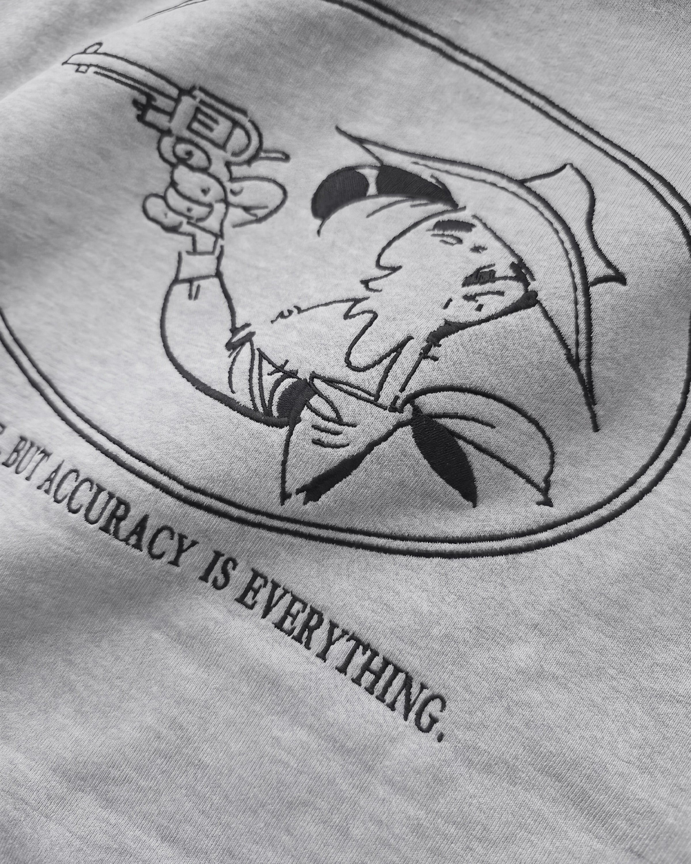 Detailaufnahme der Lucky Luke Accuracy-Stickerei auf dem grauen Half Zip. Lucky Luke mit seinem Revolver.