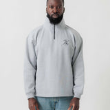 Vorderansicht eines männlichen Models im grauen Half Zip mit einer von einer Kugel durchbohrten Spielkarte auf der Brust.