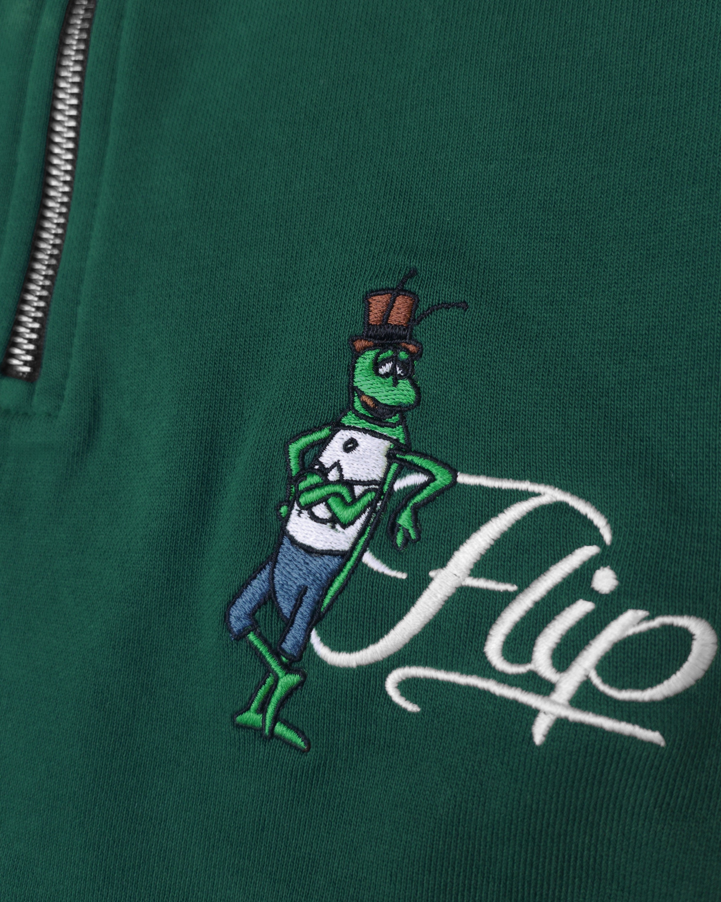 Detailaufnahme der Flip Script-Stickerei auf dem grünen Half Zip. Der lässige Flip, der sich an seinen eleganten Namensschriftzug lehnt.