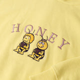 Detailaufnahme der Biene Maja Honey-Stickerei auf dem gelben Hoodie. Maja und Willi, die ihren Honig naschen.