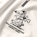 Detailaufnahme der Idéfix Happy-Stickerei auf dem weißen Half Zip. Der fröhliche Idefix mit einem Knochen.