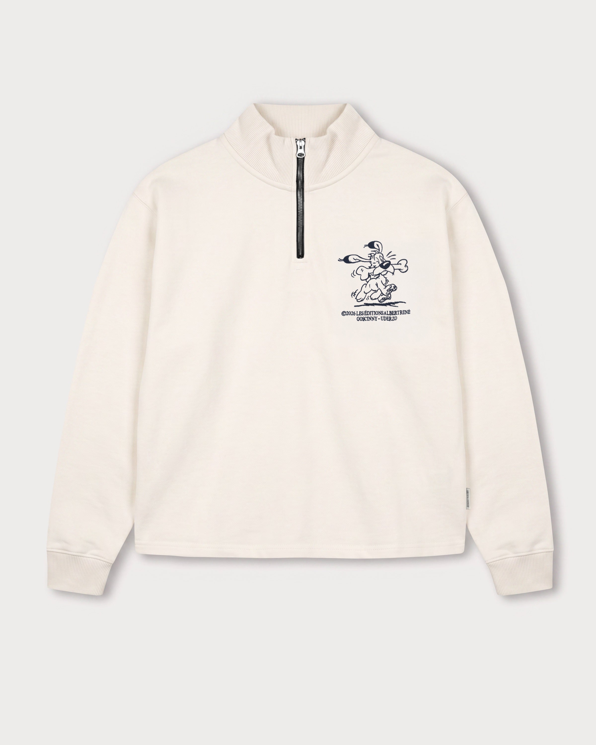 Vorderansicht des weißen Half Zips mit Idéfix Happy-Stickerei auf der Brust. Der fröhliche Idefix mit einem Knochen.