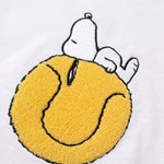 Detailaufnahme des Snoopy Tennisball-Motivs auf dem weißen Sweater. Tennisball, auf dem Snoopy tiefenentspannt relaxt.