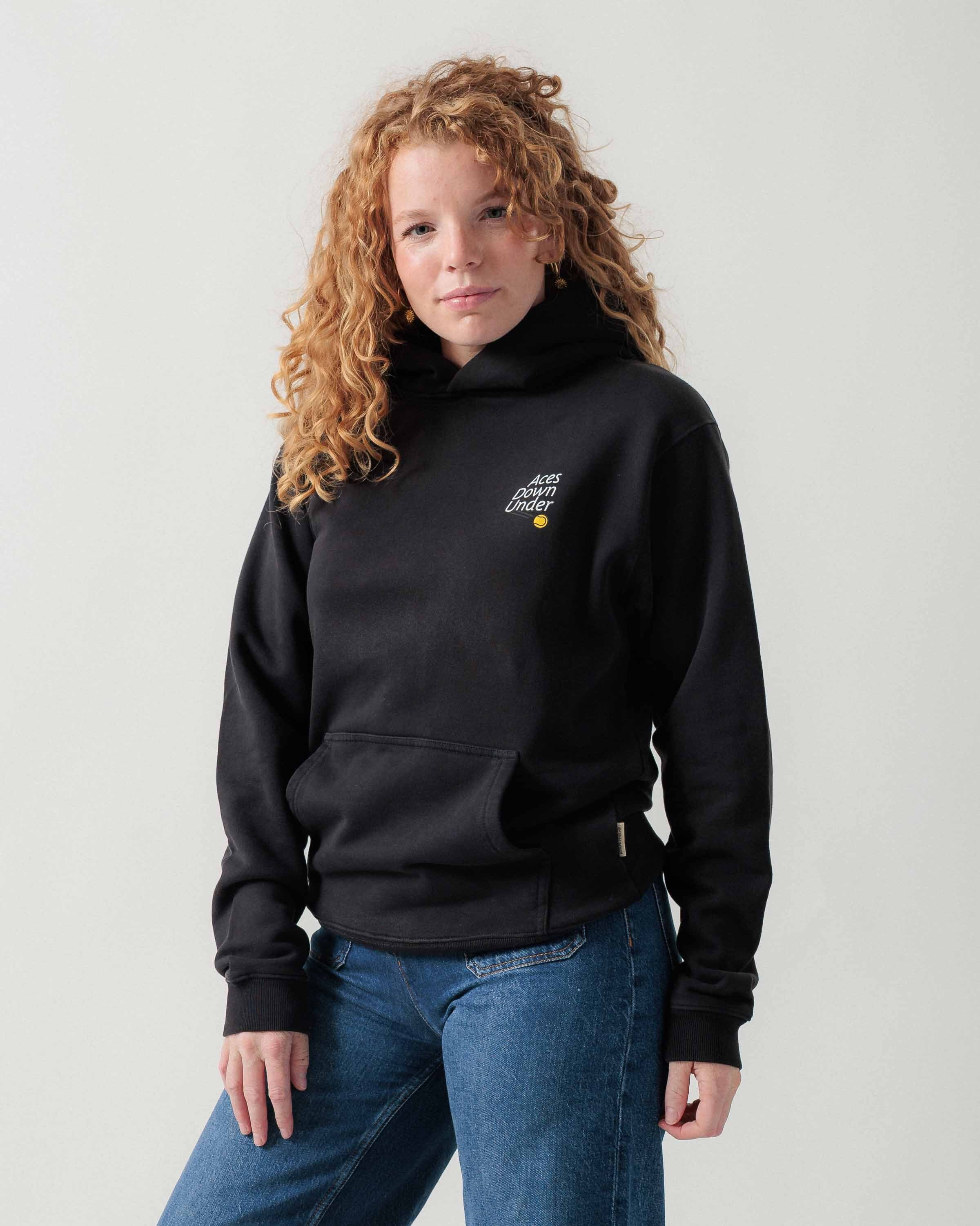 Vorderansicht eines weiblichen Models im schwarzen Street Hoodie mit kleinem Motiv auf der Brust.